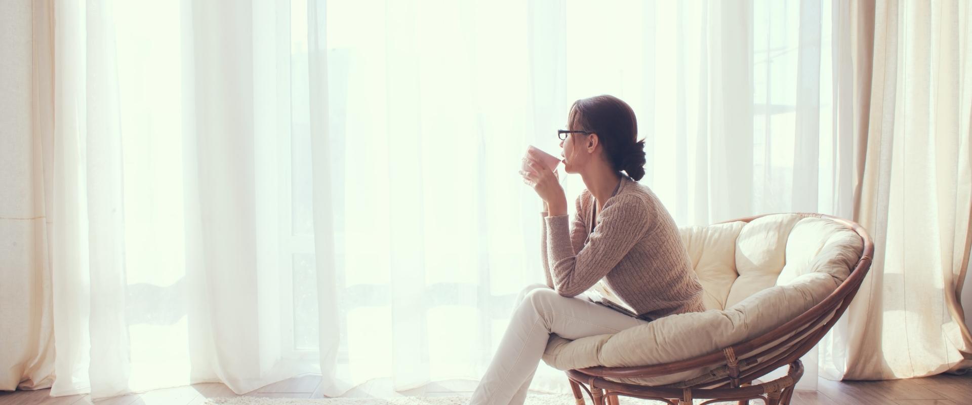 Femme assise près d’une fenêtre lumineuse, une tasse à la main, dans un moment de calme